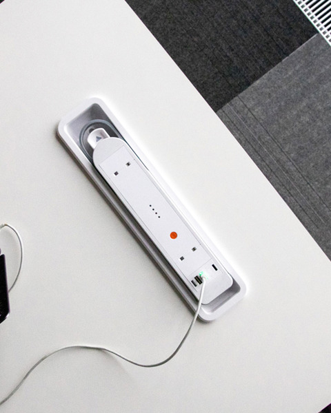 A close-up image of a person working on a laptop at a table with a white built-in battery in the tabletop