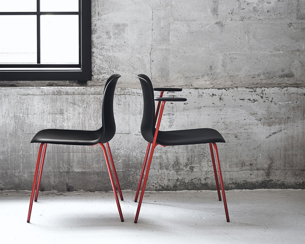 Two black SixE chairs with red frames against a grey wall with a window