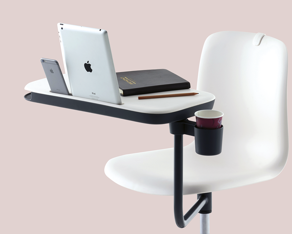 A detailed image of a white SixE Learn chair on a pink background showing a mobile phone, tablet, notebook, pencil on a writing tablet, and a cup in a cupholder